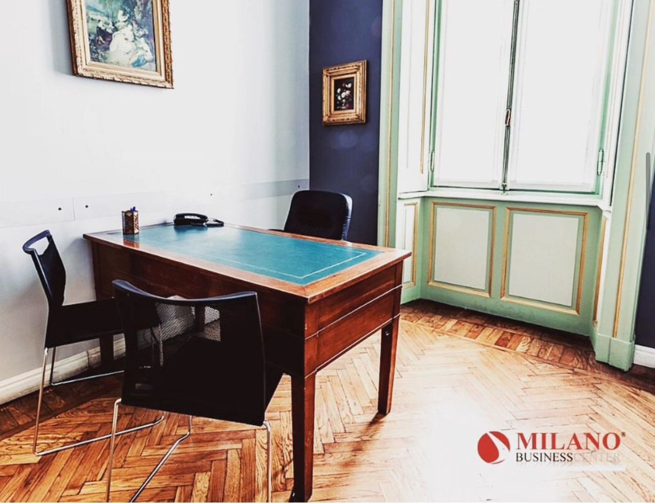 Elegant office with wooden desk, two chairs, and large window, featuring artwork on the walls.