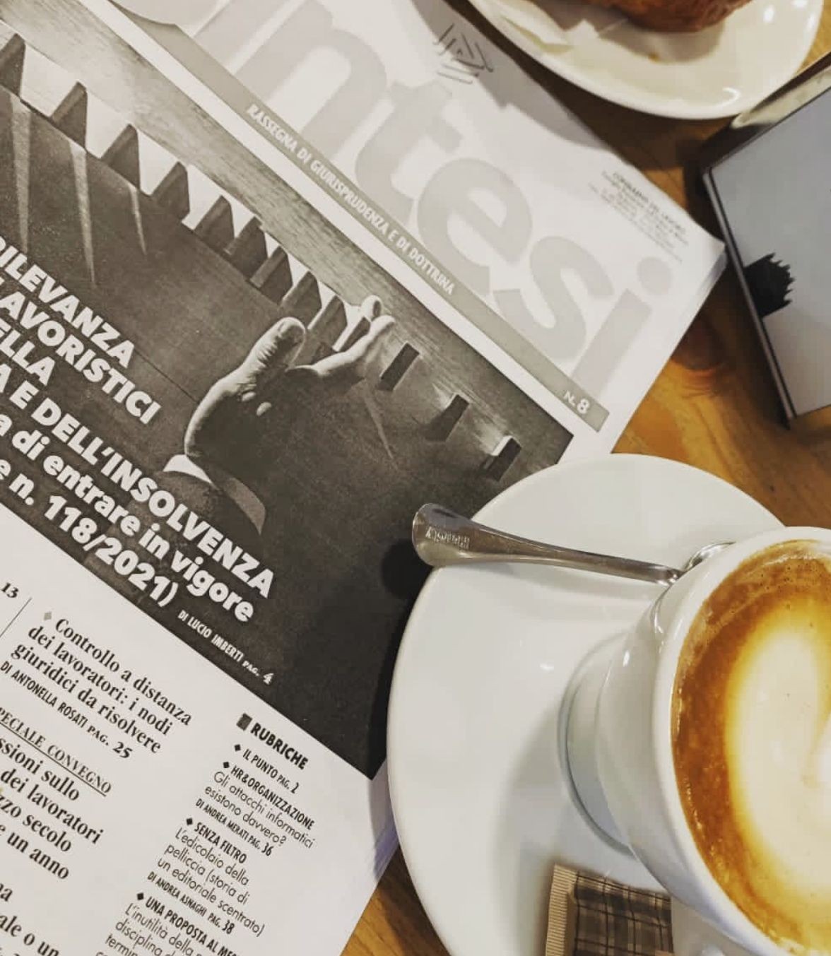 Open newspaper on a table with a cup of cappuccino and a croissant.